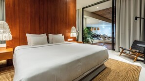 A modern hotel room with a large bed, wooden panel walls, and a view of the outdoor seating area. - Green Flow Villa 21 (Ubud)
