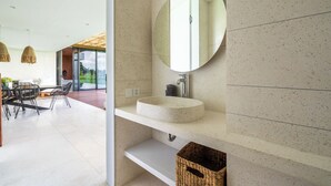 A modern bathroom with a round mirror, a white sink, and a wicker basket. - Green Flow Villa 21 (Ubud)