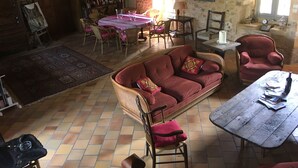 A cozy room with a wooden sofa, a dining table with chairs, a bookshelf, and a large window. - Charming cottage in Périgord: Aliénor's relay (Capdrot)