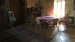 A dining area with a table set for four, surrounded by wicker chairs, a patterned rug, and a bookshelf with books and decorative items. - Charming cottage in Périgord: Aliénor's relay (Capdrot)