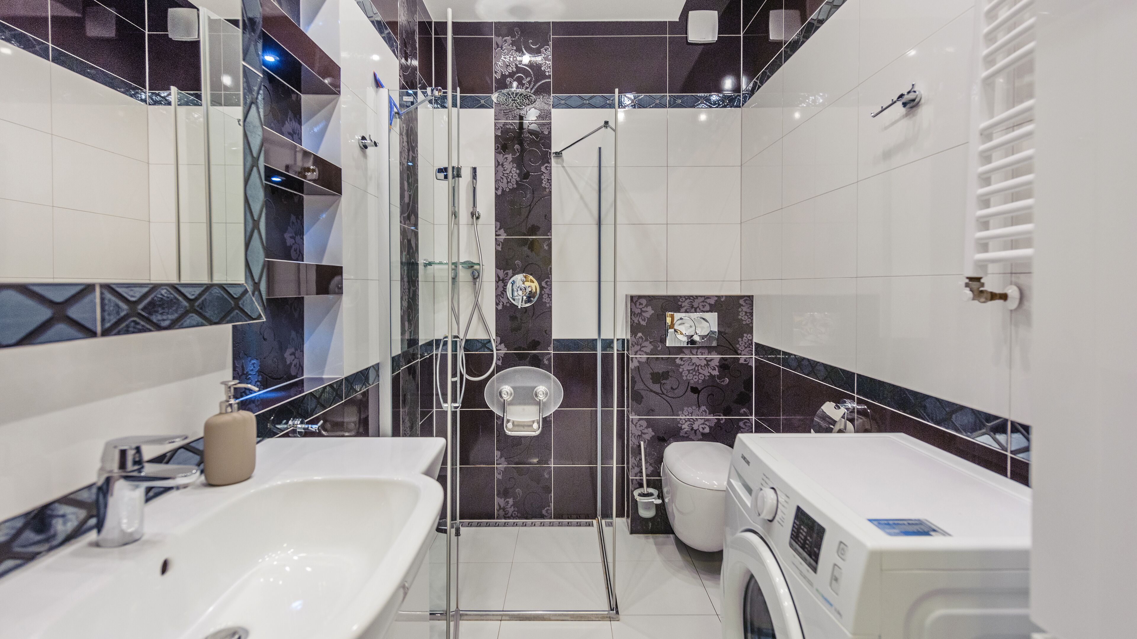 Un baño moderno con cabina de ducha de vidrio, inodoro, lavabo y lavadora.