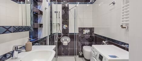Un baño moderno con cabina de ducha de vidrio, inodoro, lavabo y lavadora.