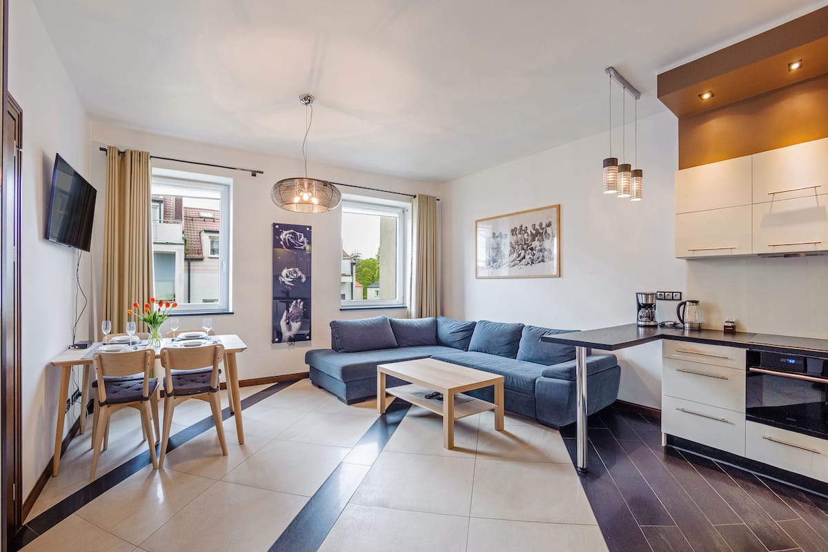 Une cuisine moderne dotée d’un four encastré, un coin repas avec une table et des chaises, et un salon avec un canapé.