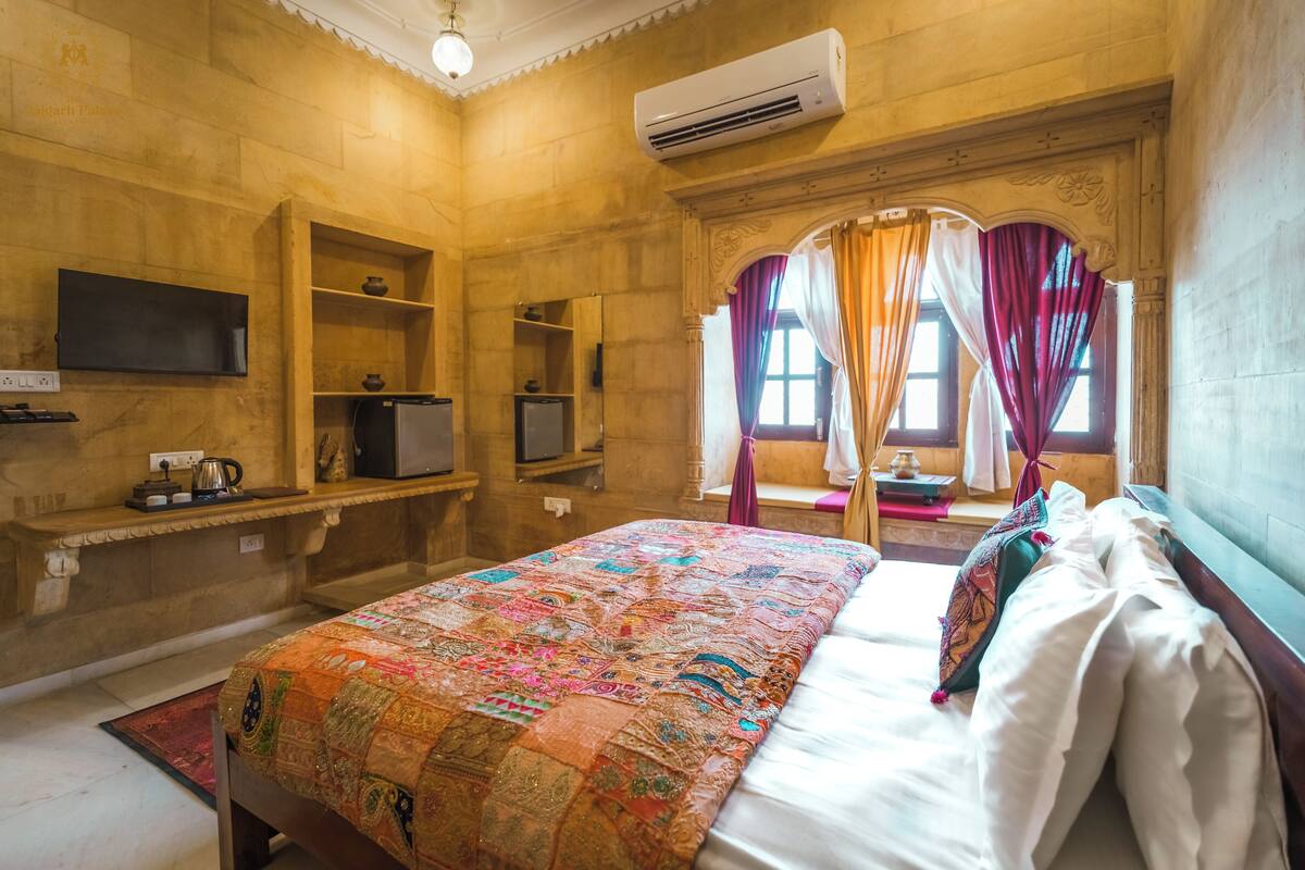 A hotel room with a large bed, a flat-screen TV, a minibar, and a window with curtains.