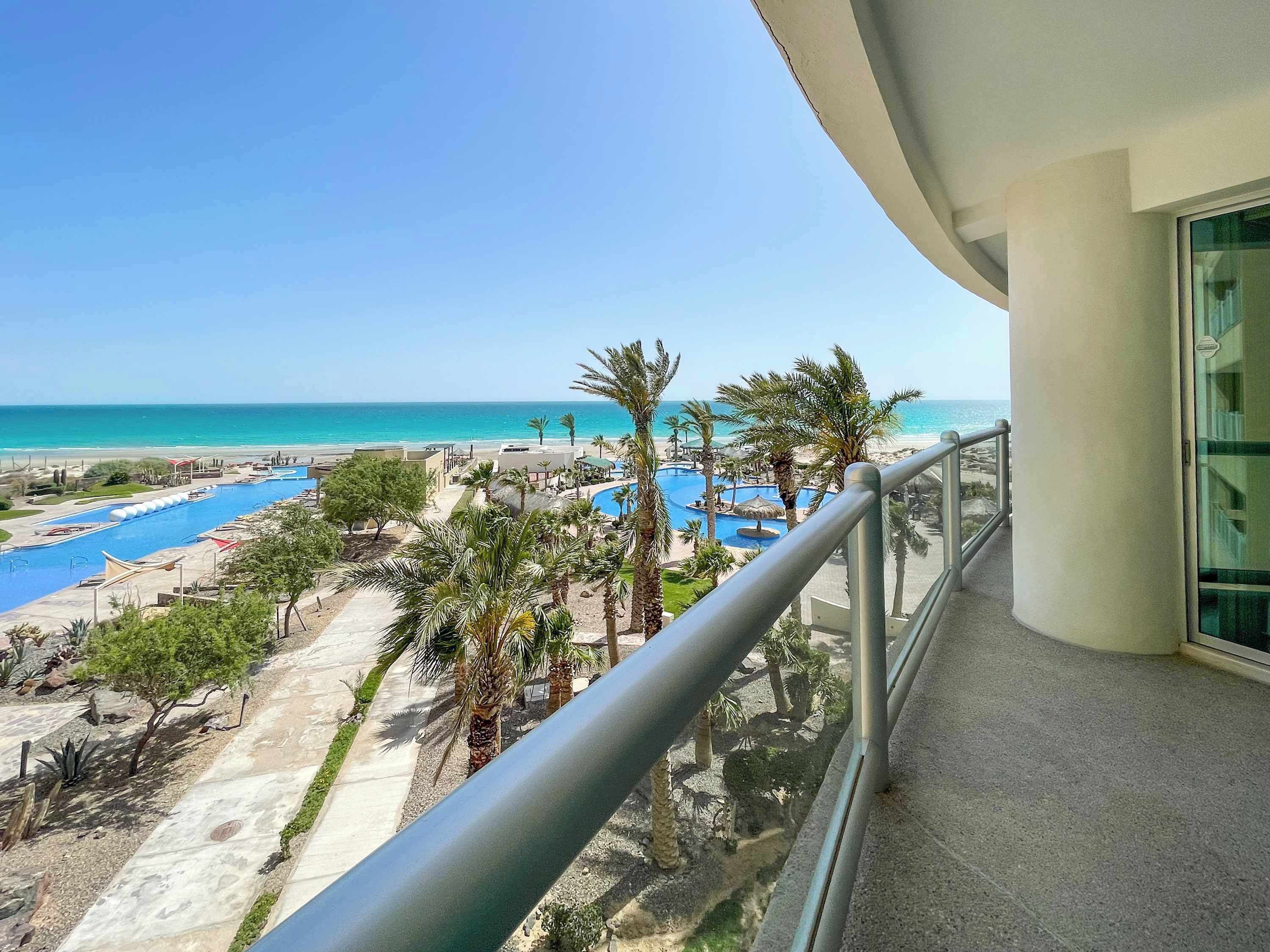 Un balcon avec vue sur une piscine, des palmiers et une plage.