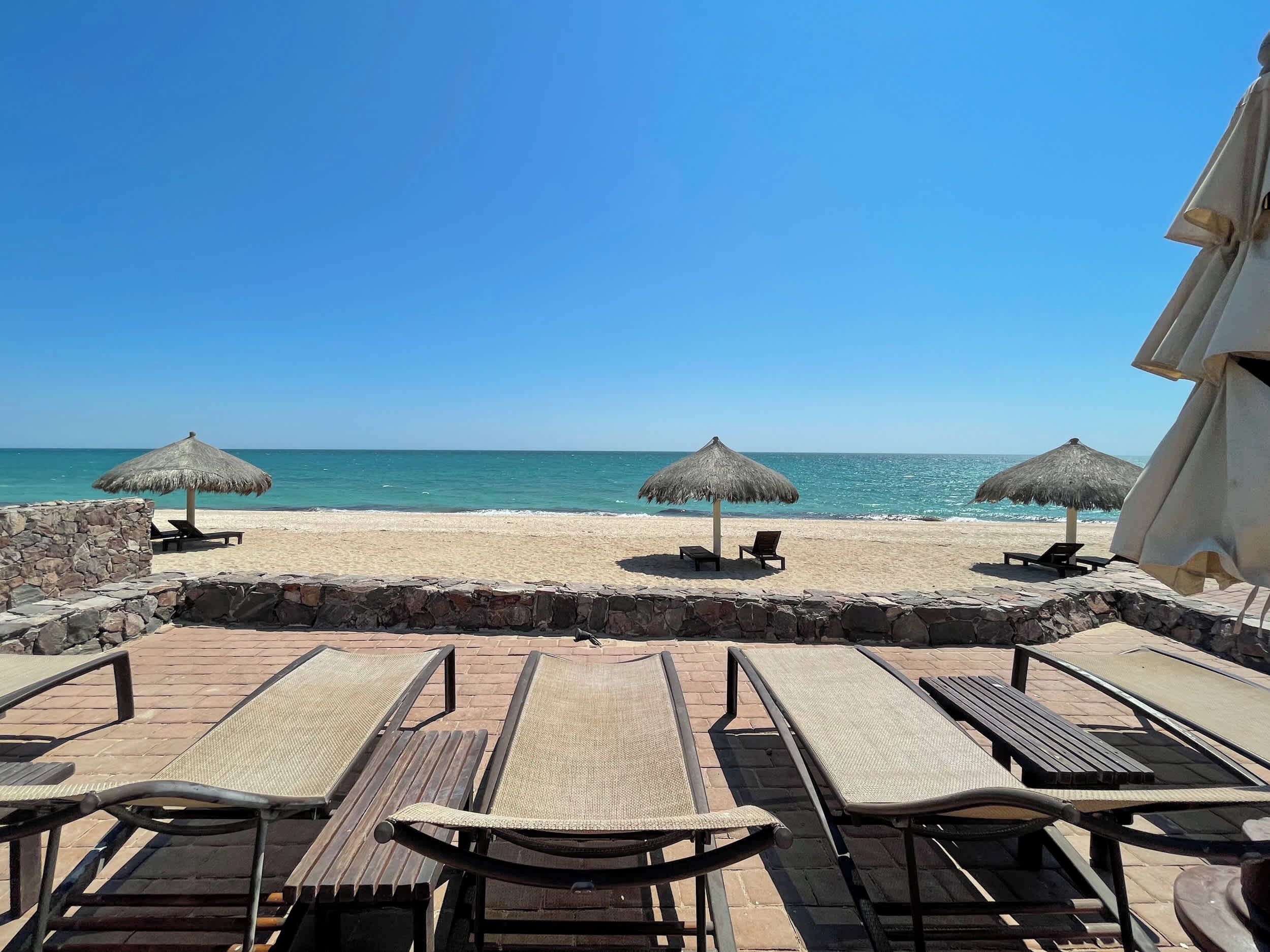 Une terrasse au bord de la plage, dotée de chaises longues et de parasols en chaume, avec vue sur la mer.