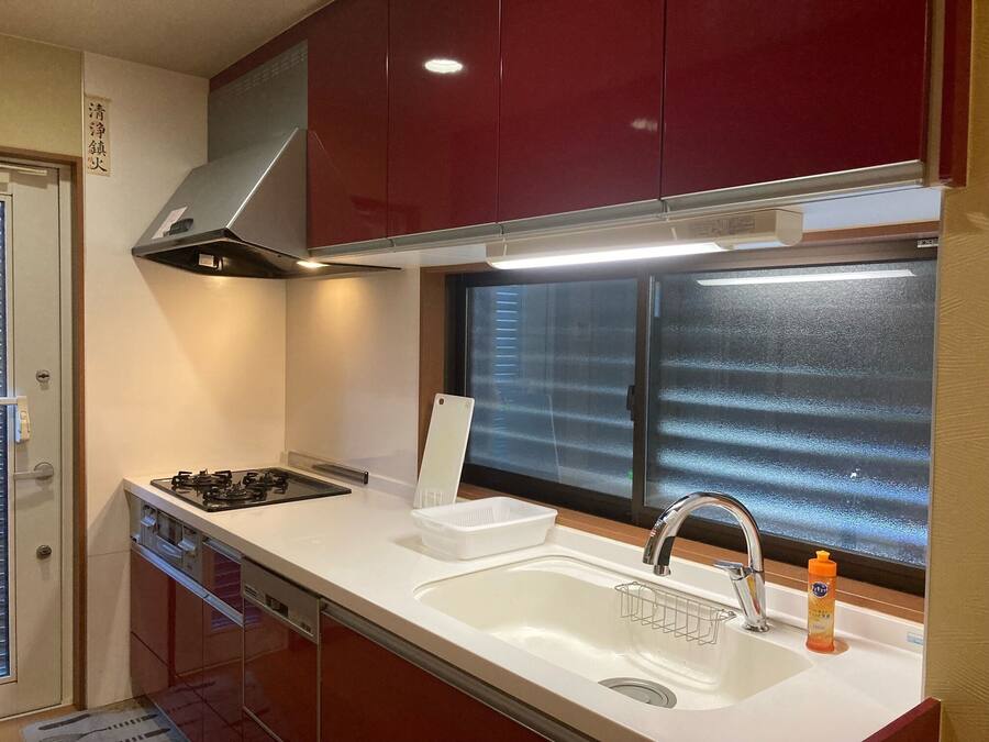 A compact kitchen with a gas stove, a stainless steel range hood, a white sink with a faucet, and a window with frosted glass.