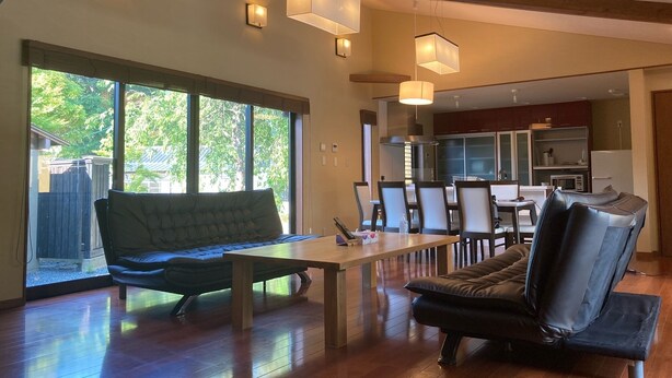 Un salón amplio con suelo de madera, un ventanal grande y una mesa de comedor con sillas.