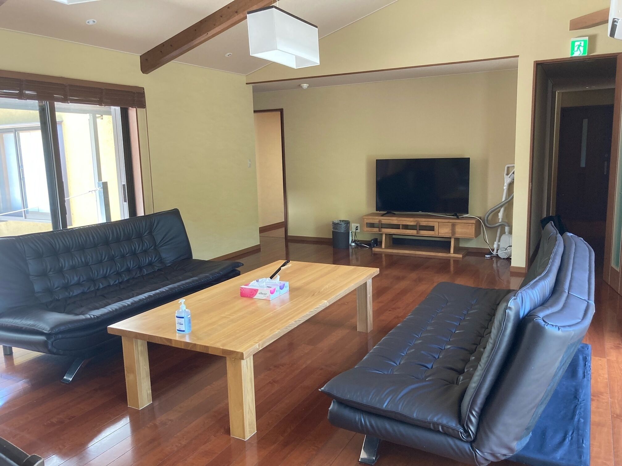 A living room with a wooden coffee table, two black sofas, a TV on a wooden stand, and a wooden floor.