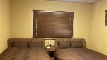 A bedroom with two single beds, a nightstand with a lamp, and a window with blinds.