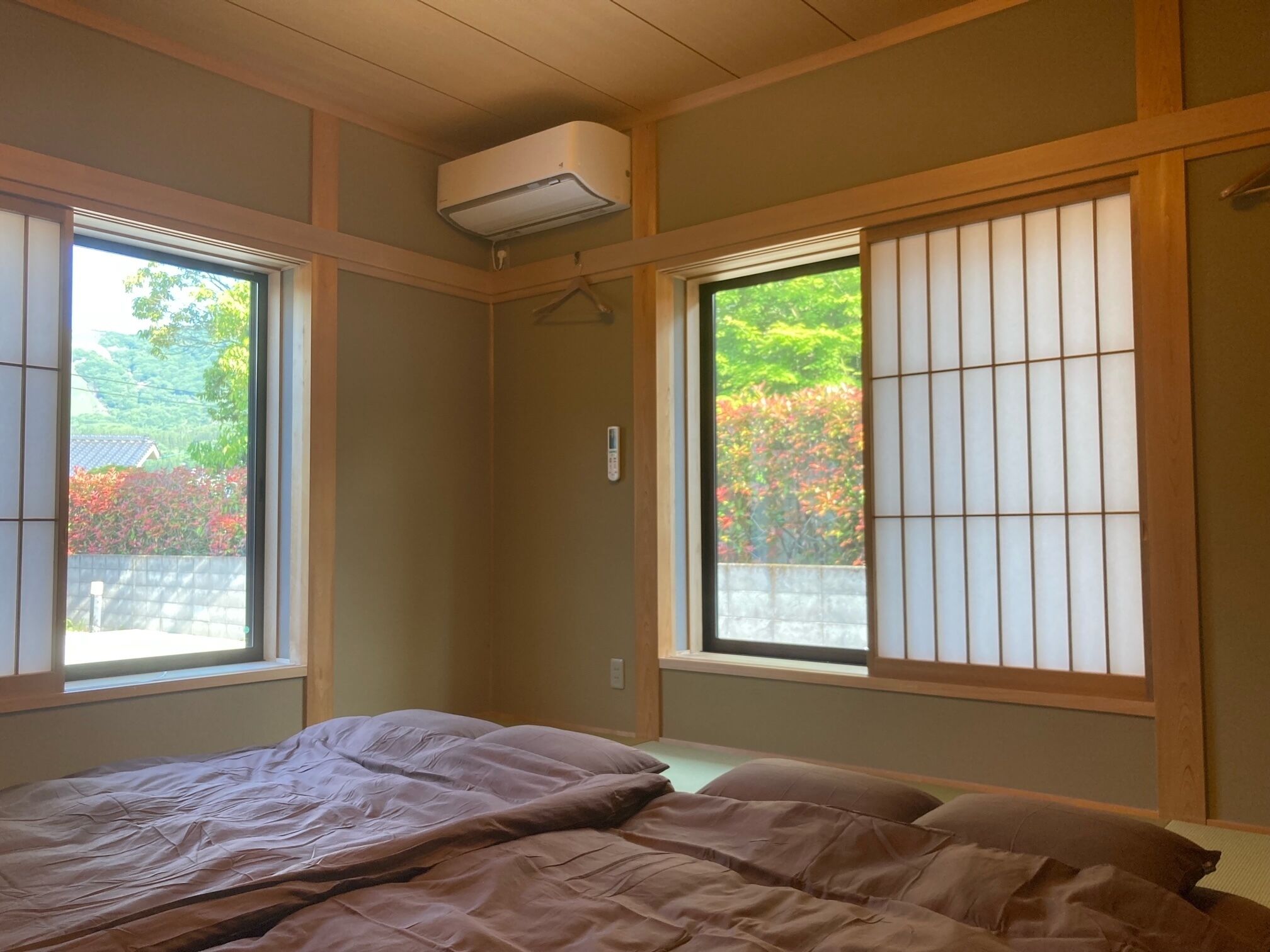 Ein Schlafzimmer mit Bett, einem Fenster mit Blick auf Bäume und einer Klimaanlage.