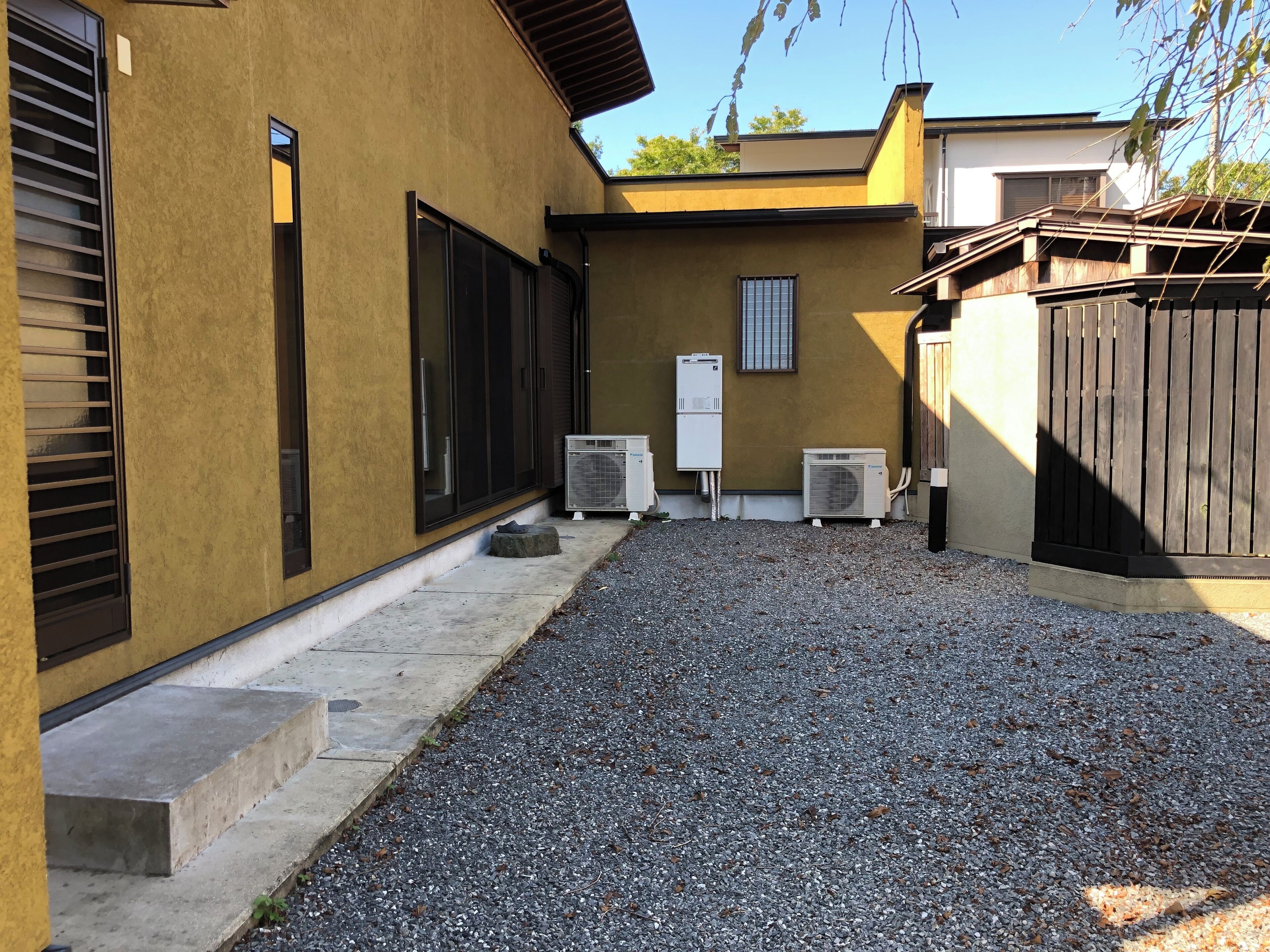 A building with a yellow exterior, a gravel driveway, and two air conditioning units.