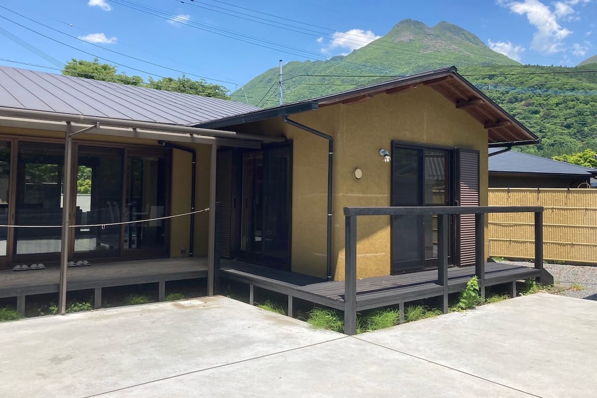 A small, single-story building with a metal roof and a wooden deck. It has a black door and a small porch area.