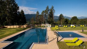 A swimming pool with multiple lanes, surrounded by green lawn and trees. - EuroParcs Pressegger See (Hermagor-Pressegger See)