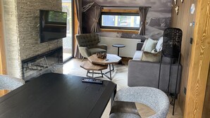 A cozy living room with a stone wall, a fireplace, a TV, a sofa, a coffee table, and a dining table. - EuroParcs Pressegger See (Hermagor-Pressegger See)