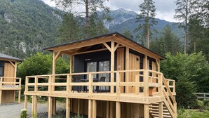 A wooden cabin with a balcony, surrounded by a forest and mountains. - EuroParcs Pressegger See (Hermagor-Pressegger See)