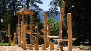 A wooden play structure in a park with a rope bridge and a small wooden shelter. - EuroParcs Pressegger See (Hermagor-Pressegger See)