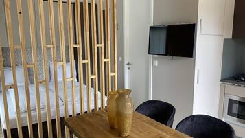 A modern bedroom with a wooden bed frame, a TV mounted on the wall, and a wooden dining table with chairs.
