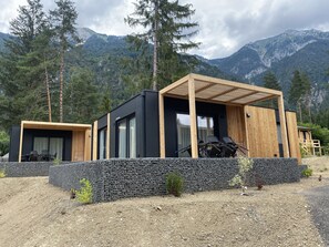 A modern cabin with a wooden pergola and a black exterior, surrounded by a rocky landscape and mountains. - EuroParcs Pressegger See (Hermagor-Pressegger See)