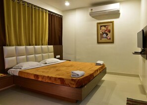 Una habitación de hotel con cama, televisión, aire acondicionado y un cuadro en la pared.