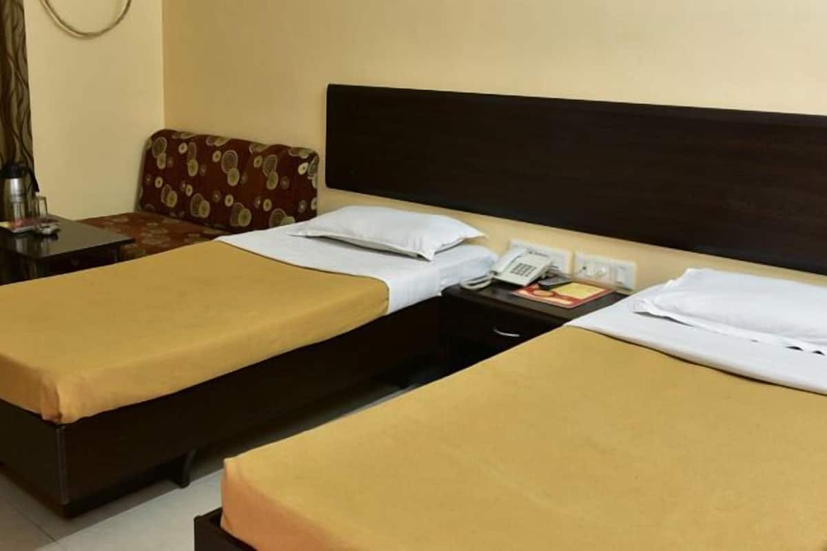 A hotel room with two single beds, a desk, a chair, a small table with a phone and a book, and a curtain.