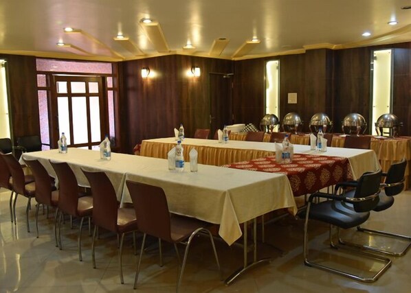Un salón de conferencias con largas mesas, sillas y botellas de agua.