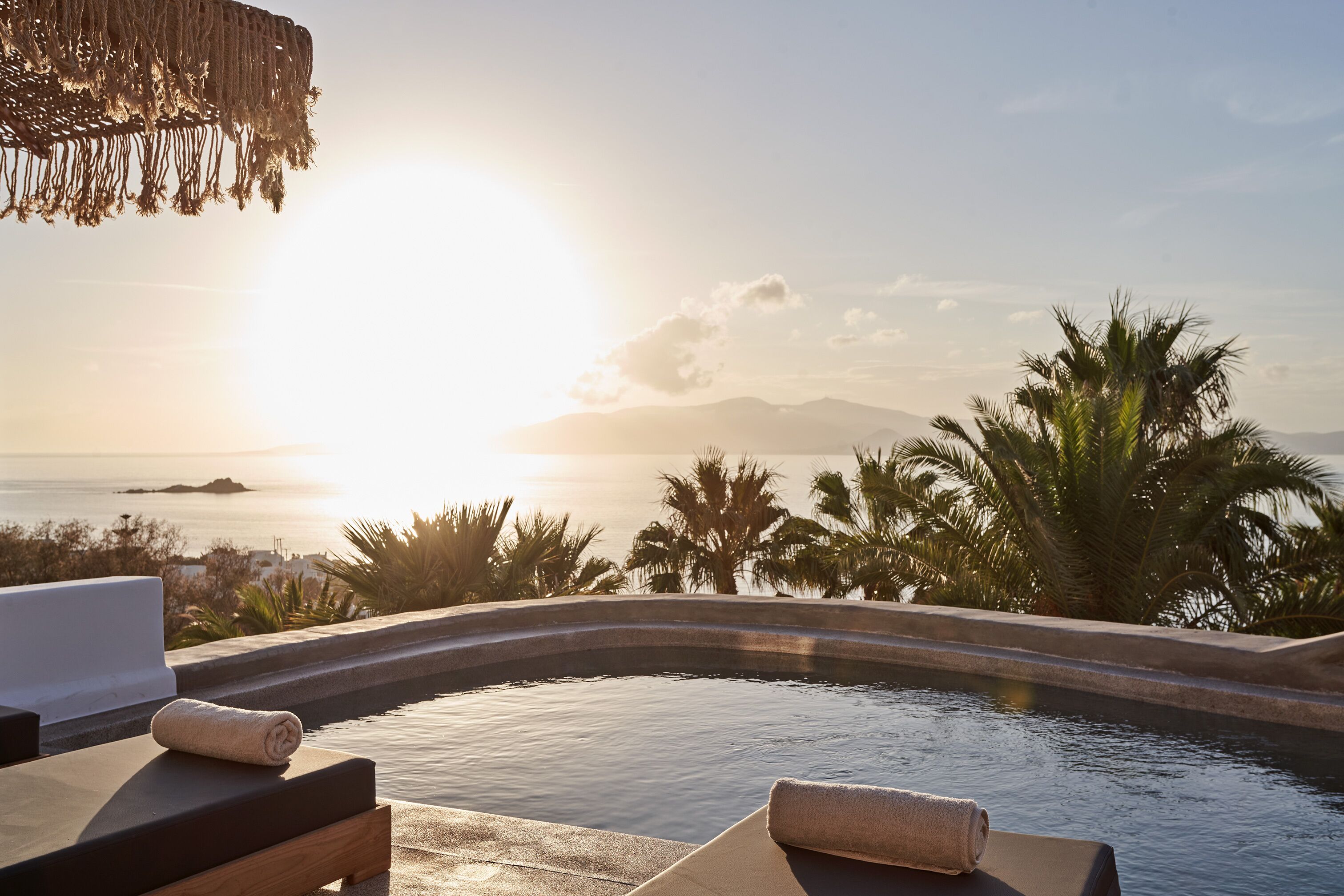 A poolside area with lounge chairs and a view of the ocean at sunset.