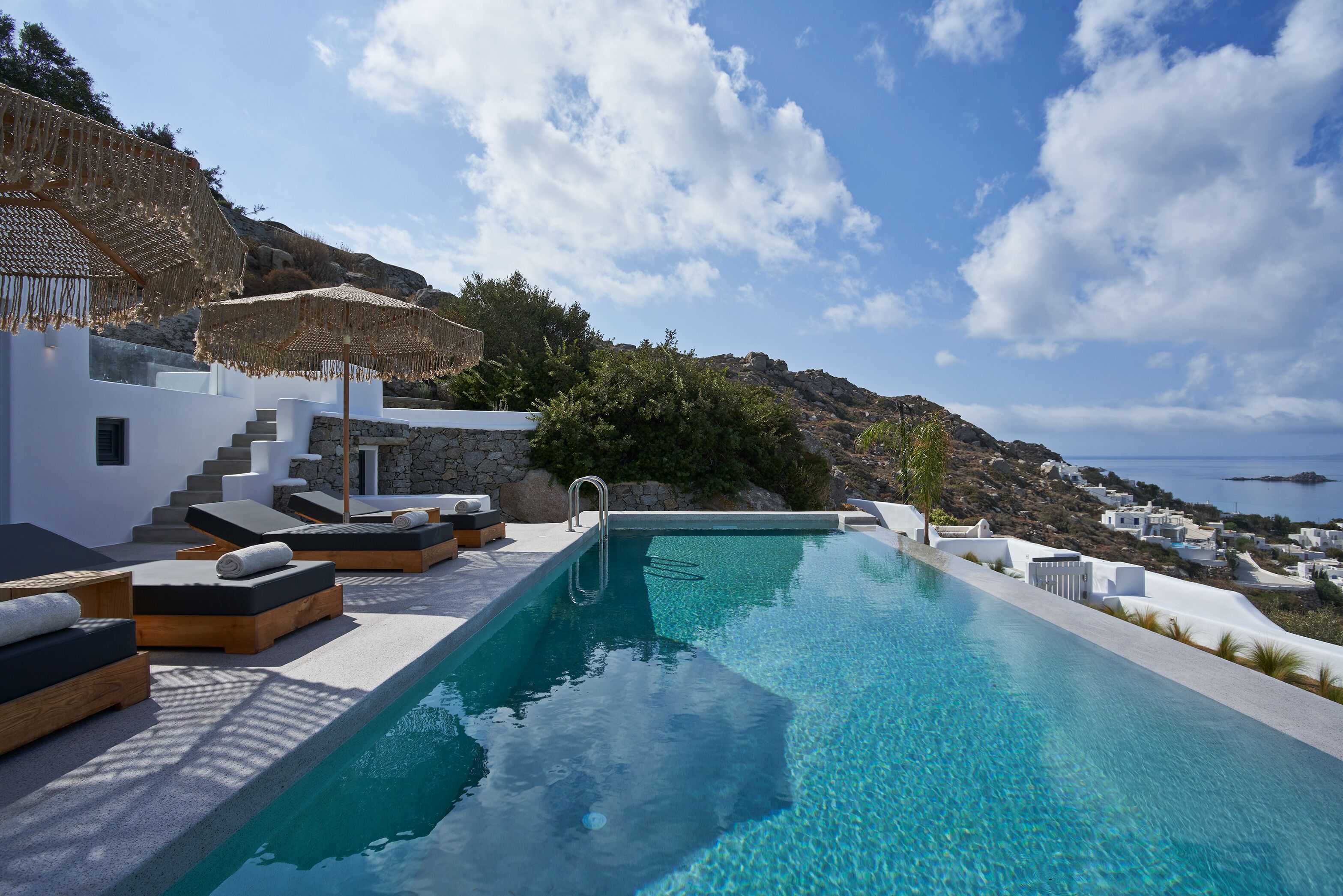 Zona junto a la piscina con sillones de descanso, una escalera y vista al mar.