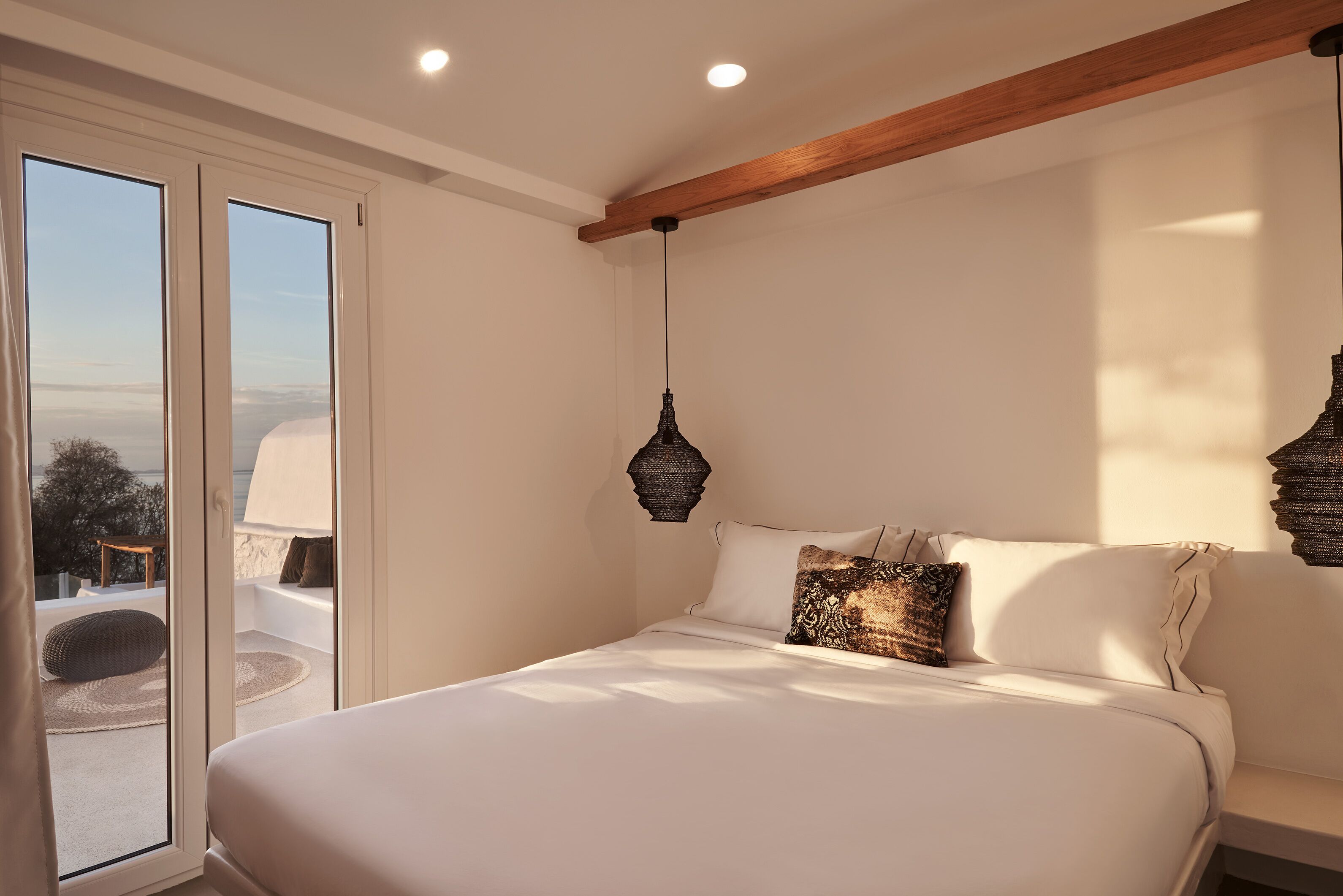Camera da letto con un letto grande, vista su una zona esterna tramite una porta scorrevole e trave in legno al soffitto.
