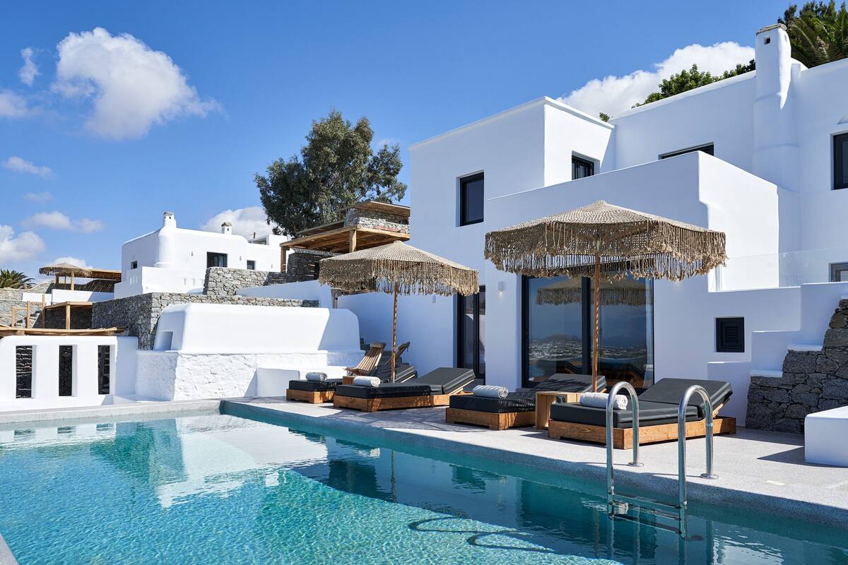 A pool area with lounge chairs and umbrellas, surrounded by white buildings with stone accents.