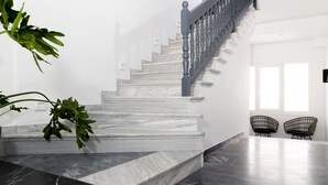 A staircase with marble steps and a wooden railing, leading to a room with a large window and two black chairs. - Naxian Memories (Naxos)