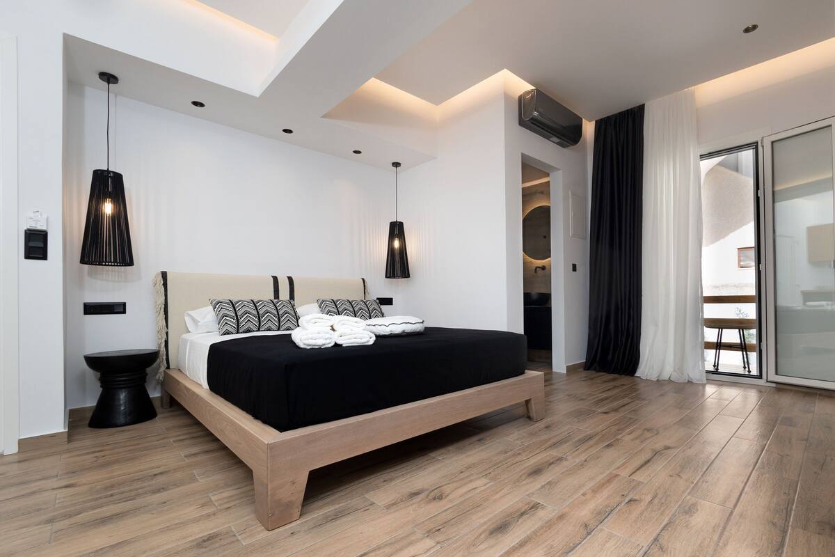 Ein modernes Schlafzimmer mit einem Holzbett, schwarzer Bettwäsche und Pendelleuchten.