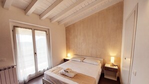 A bedroom with a bed, two bedside tables, a window with curtains, and a wooden wall. - Bright apartment with pool and amazing view (Mezzane)
