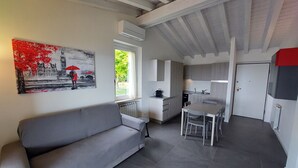 A modern living room with a grey sofa, a dining table with chairs, and a kitchen area with grey cabinets and a white countertop. - Bright apartment with pool and amazing view (Mezzane)