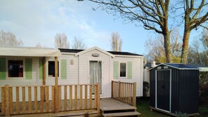 Een rij mobiele woningen met een houten terras en een tuinhuis.