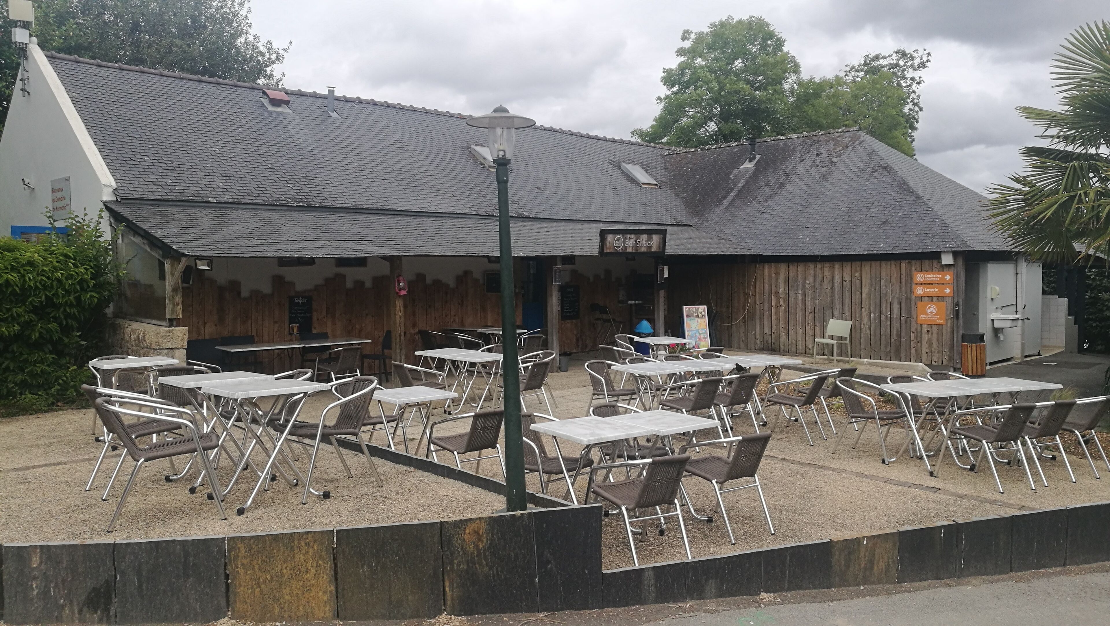 Un café en plein air avec des tables et des chaises, un bâtiment en bois doté d’un toit en pente et une enseigne indiquant qu’il s’agit d’un restaurant.