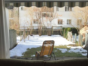 Una vista dalla finestra, con una sedia in primo piano, un cortile innevato e un edificio sullo sfondo.