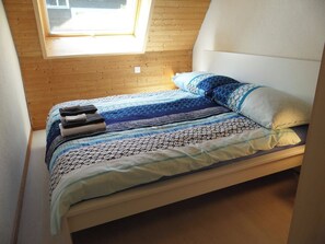 Un letto con una coperta e dei cuscini decorati, una finestra sopra e una parete in legno.
