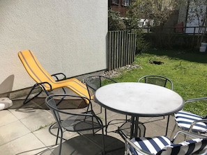 An outdoor patio with a round table and chairs, a yellow lounge chair, and a small garden area. - Hostattstrasse 20 Appartement/Fewo 4-Bettwohnung by Interhome (Engelberg)