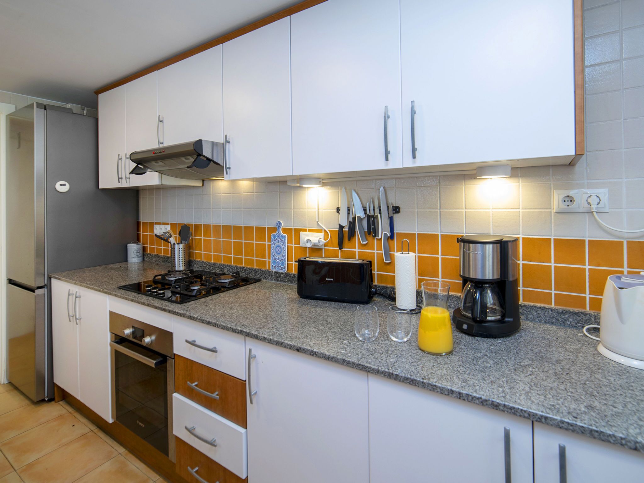 Une cuisine moderne avec des meubles blancs, une cuisinière à gaz, une machine à café et un grille-pain.