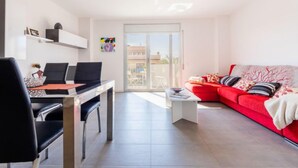Un salon moderne avec un canapé rouge, un coin repas comprenant une table et des chaises, et une vue sur l’extérieur à travers une porte vitrée.