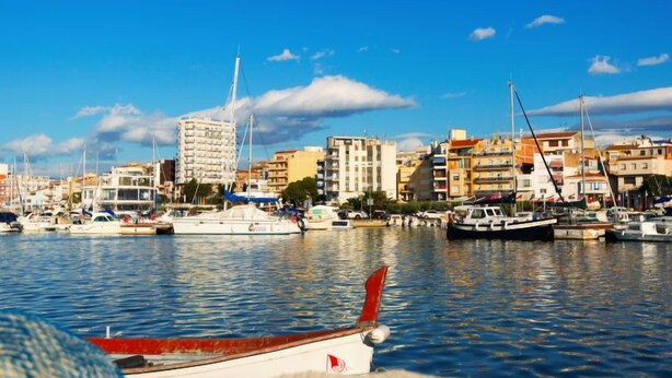 Un port de plaisance avec des bateaux amarrés, un bâtiment doté d’une haute flèche et un ciel bleu dégagé.