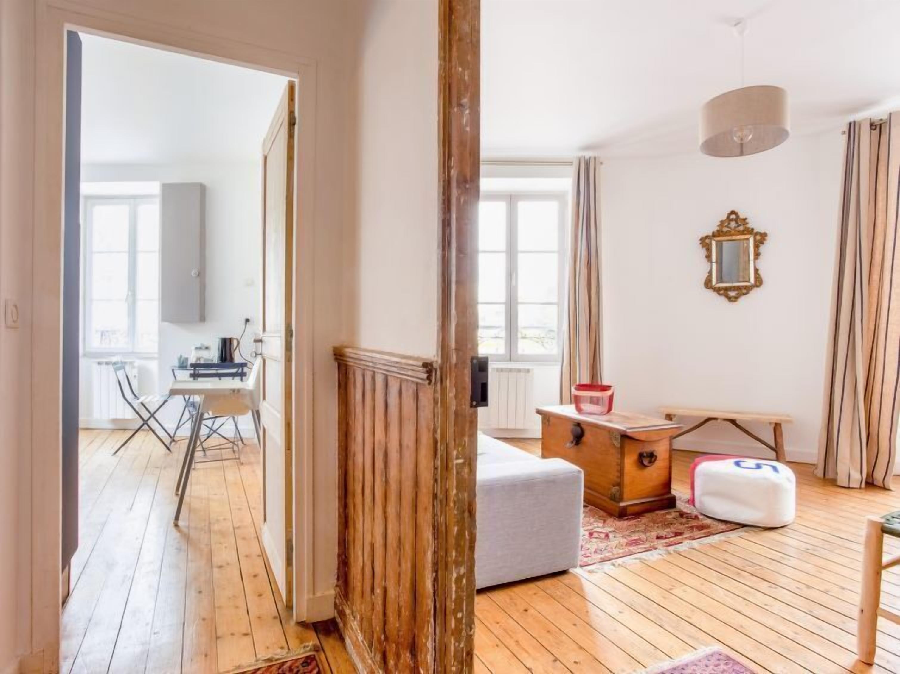 Une pièce avec un plancher en bois, un canapé blanc, une commode en bois, une petite table et un miroir au mur.