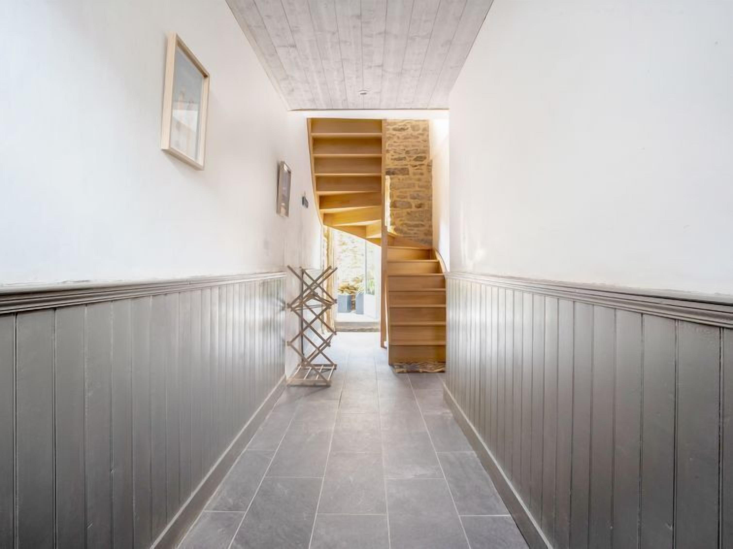 A hallway with a wooden staircase leading to a stone wall.