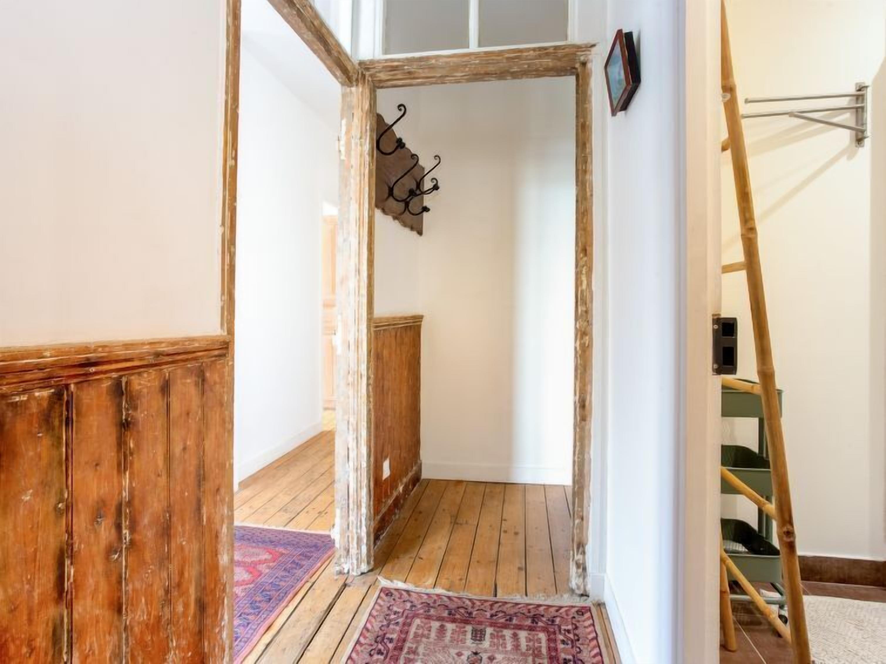 Ein Zimmer mit Holzboden, einem Holztürrahmen, einem kleinen Teppich und einer an der Wand angelehnten Leiter.