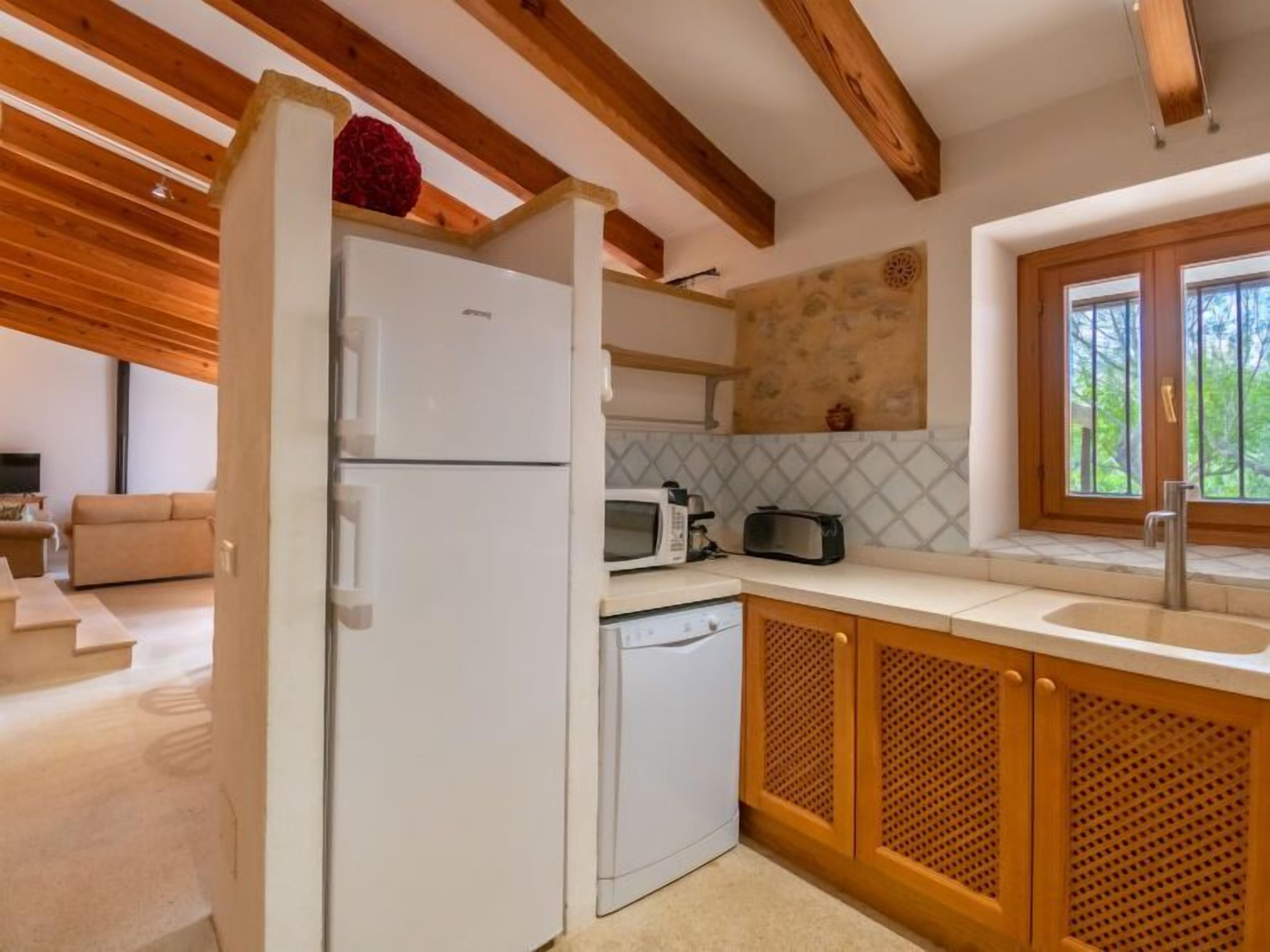 Eine kompakte Küche mit Holzbalken, einem weißen Kühlschrank, einer Mikrowelle, einem Toaster und einem Spülbecken mit Fenster darüber.