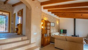 A living room with a stone wall, wooden beams, a staircase, a sofa, and a television. - Capella Rubi by Interhome (Artà)