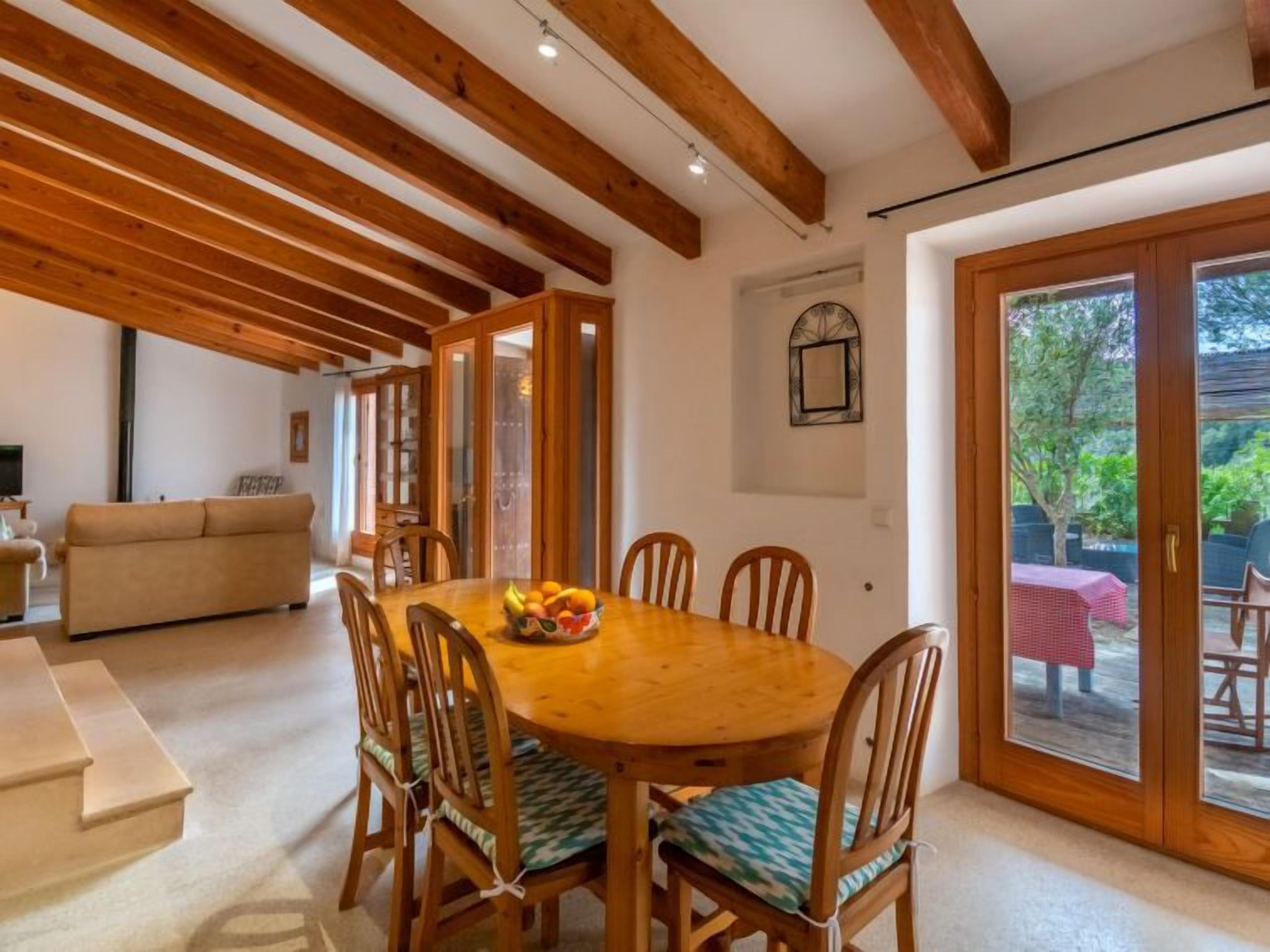 Un coin repas avec une table et des chaises en bois, un saladier rempli de fruits et une vue sur l’extérieur grâce à des portes vitrées.