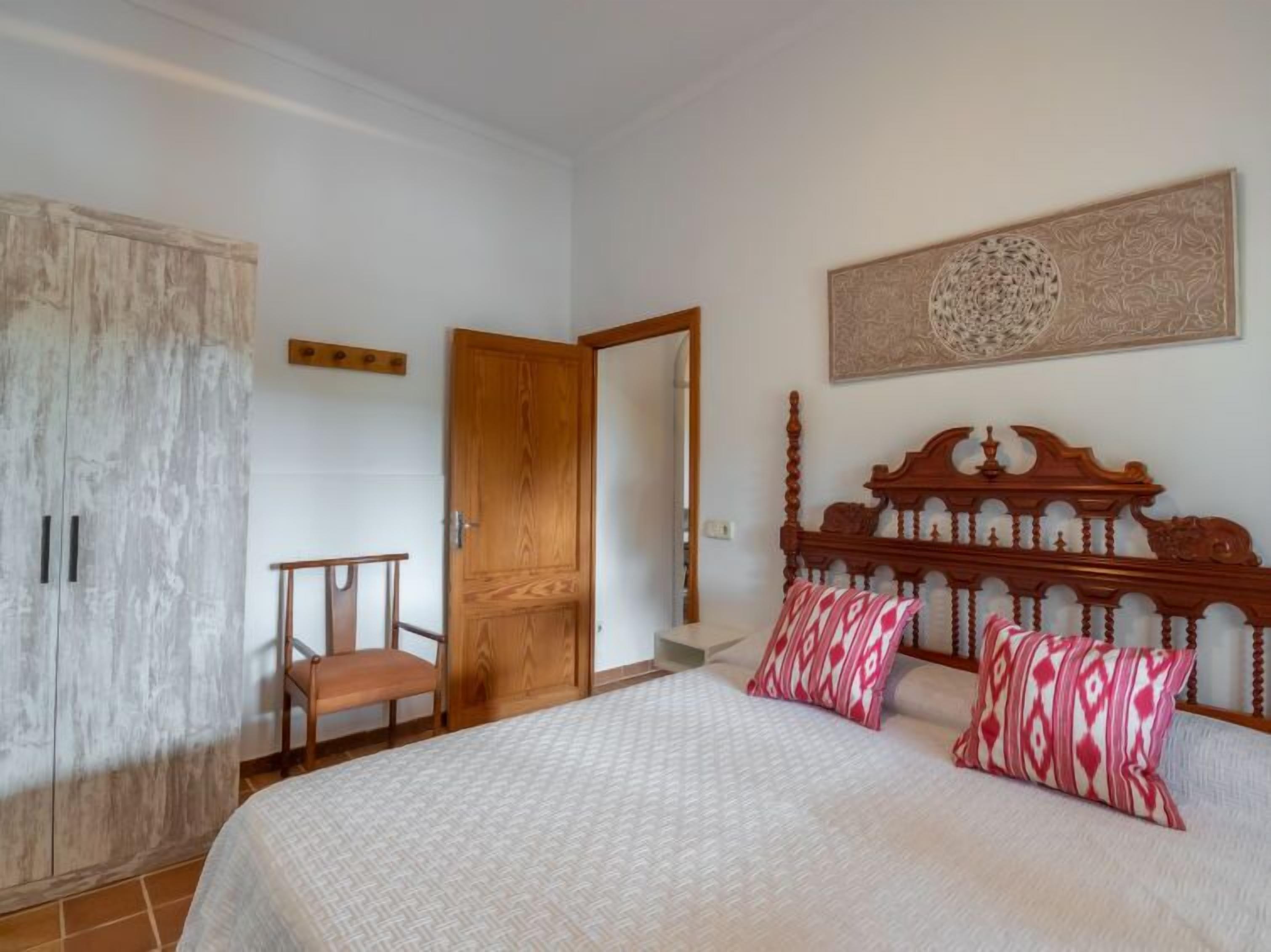 Un dormitorio con cama, armario de madera, una silla y una puerta.