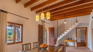 A spacious dining area with a wooden table and chairs, a bowl of fruit, and a staircase leading to another level. - Capella Rubi by Interhome (Artà)